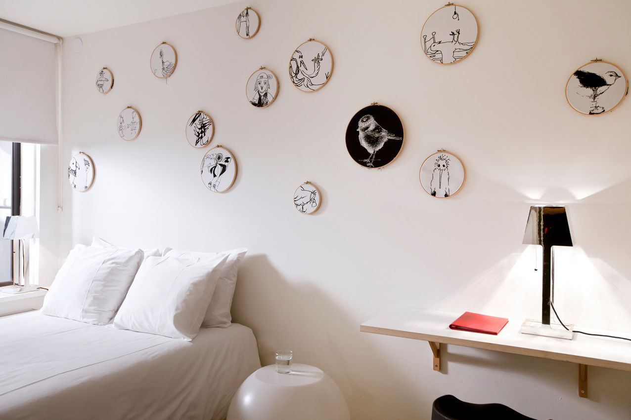 White bedroom with bed, artwork on wall, small table, lamp.