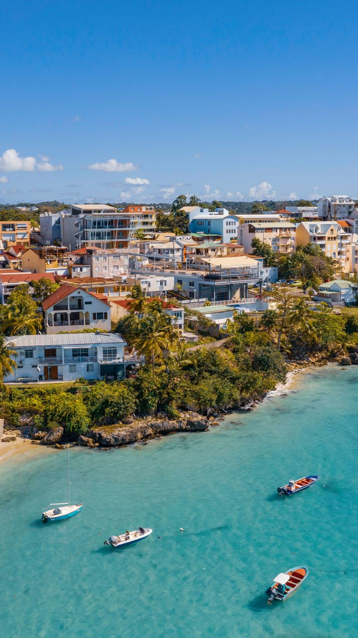Ville côtière aux bâtiments colorés, bateaux sur une eau turquoise et ciel d'un bleu éclatant.