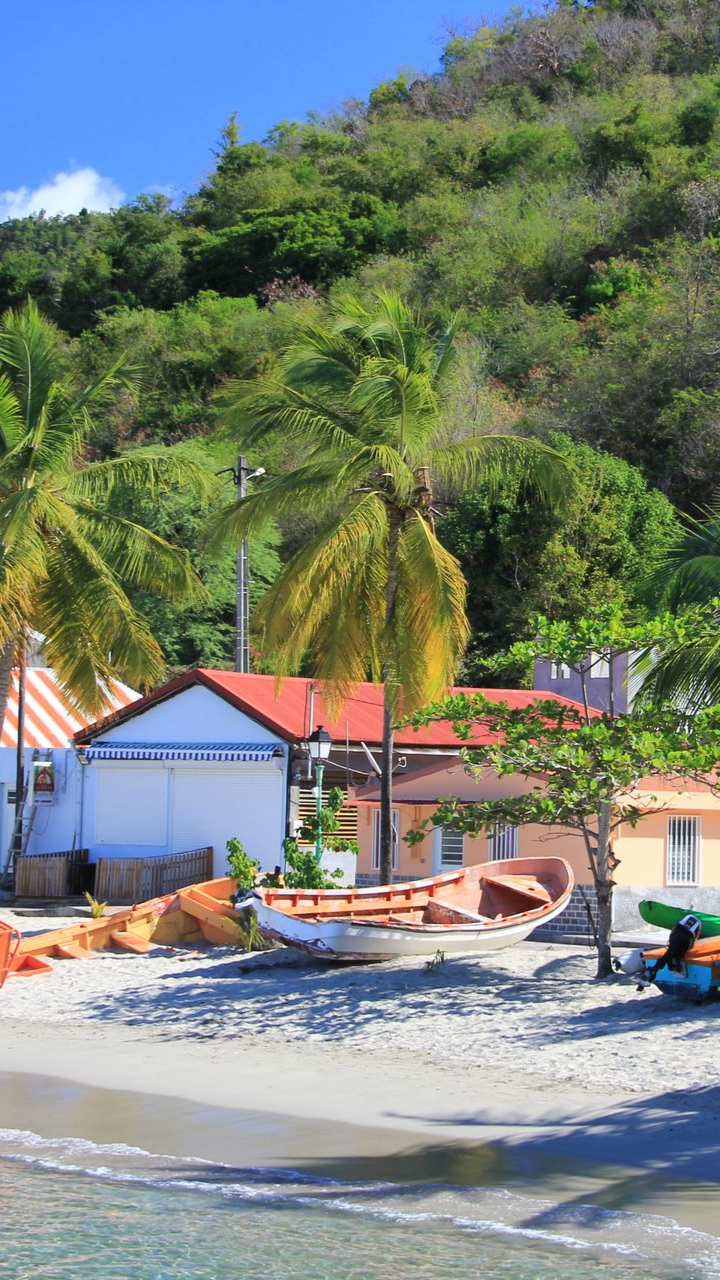 Des maisons en bord de mer aux toits rouges se dressent à côté d'une plage de sable fin, avec les collines verdoyantes en arrière-plan.