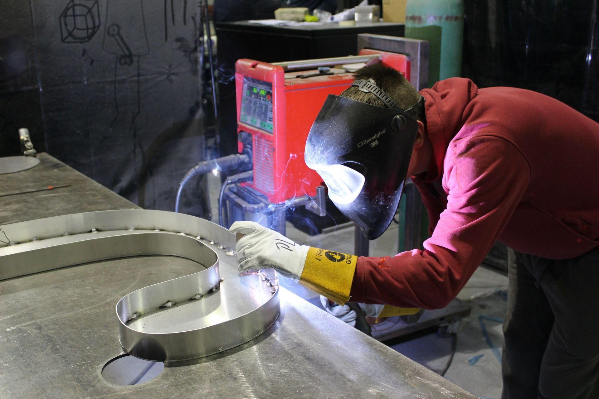 Soudeur dans un atelier utilisant une machine à souder sur une pièce métallique courbée.