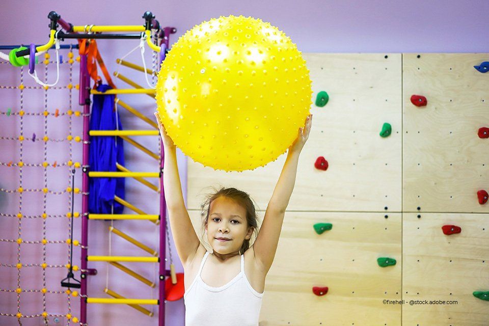 Kind hält einen großen, gelben Ball hoch
