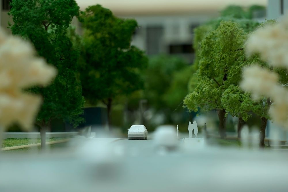 Calle de la ciudad que parece un juguete, con árboles borrosos, un coche blanco y pequeñas figuras en la distancia.