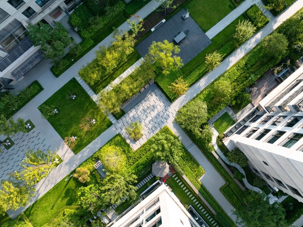Vista aérea de un patio urbano ajardinado con senderos, árboles y edificios circundantes.