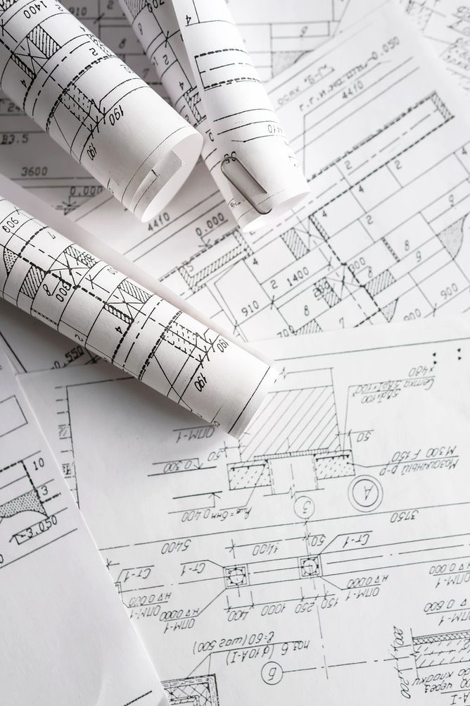 Planos arquitectónicos enrollados sobre un escritorio con hojas de dibujo técnico debajo.