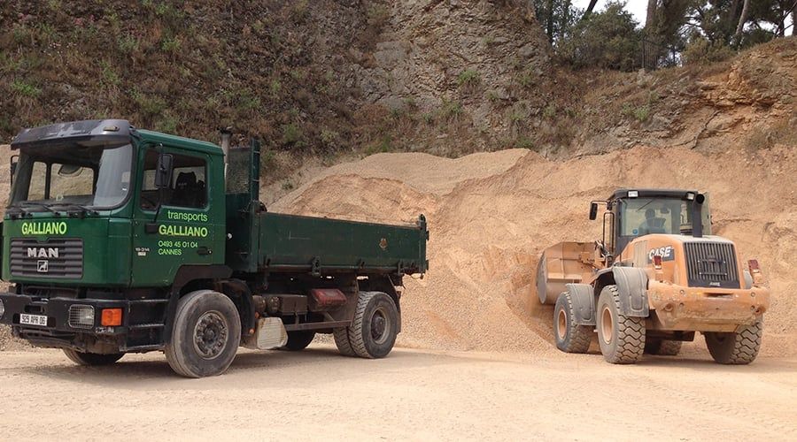 Un camion-benne vert et une chargeuse orange à côté d'un tas de terre dans une carrière.