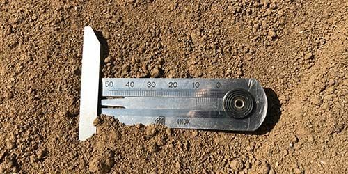 Un instrument de mesure en argent partiellement enfoui dans de la terre brune.