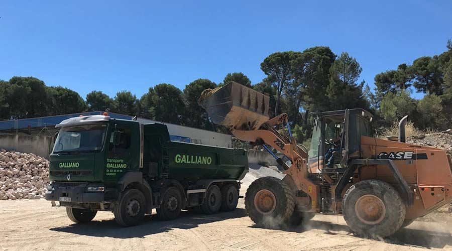 Une chargeuse sur pneus déverse des matériaux dans la benne d'un camion Galliano vert sur un chantier extérieur.