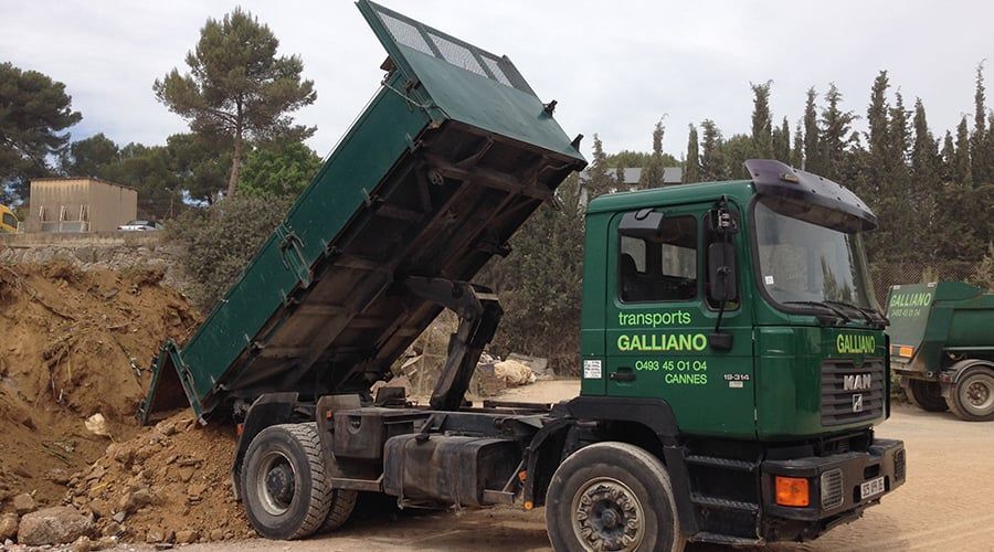 Camion-benne vert déchargeant de la terre, à l'extérieur.