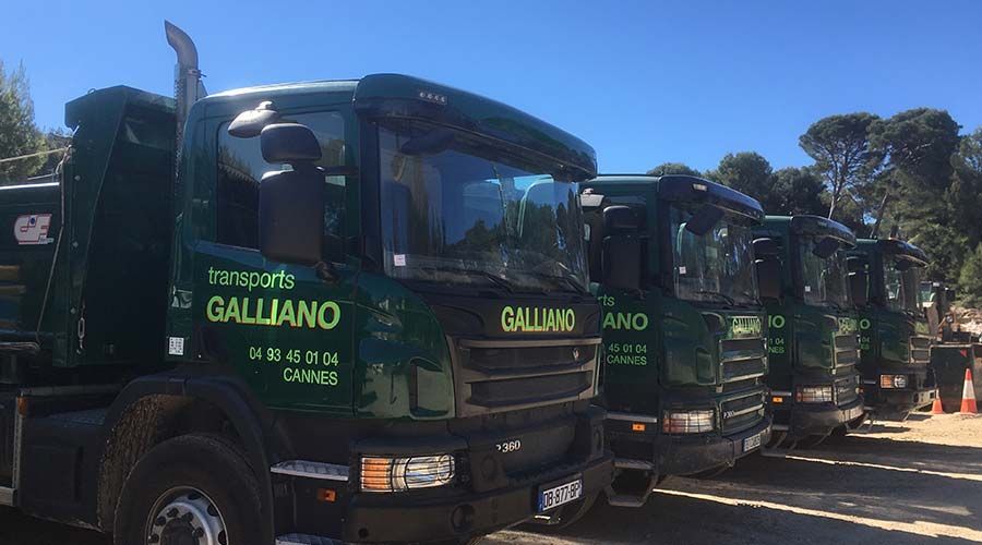 Une rangée de camions de transport Galliano verts, stationnés à l'extérieur par une journée ensoleillée.