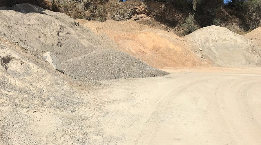 Des tas de gravier et de sable de différentes couleurs dans une carrière. Un chemin de terre se trouve au premier plan.
