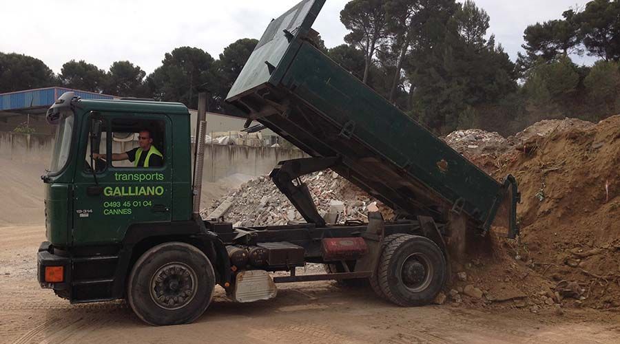 Camion-benne vert déchargeant de la terre, homme dans la cabine, en extérieur.