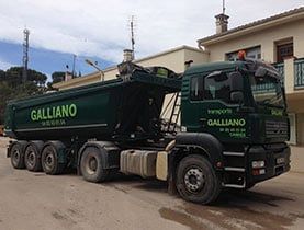 Camion-benne Galliano vert foncé à plateau surélevé sur une rue pavée.