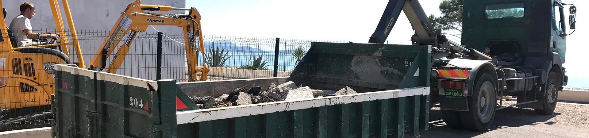 Une excavatrice charge des débris dans un camion-benne, près de l'eau.