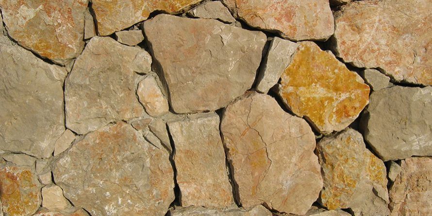 Gros plan sur un mur de pierre. Les pierres présentent différentes nuances de beige et de brun, avec un mortier gris entre elles.