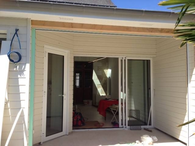 Des portes coulissantes en verre à encadrement blanc s'ouvrent sur un patio, laissant entrevoir un lit recouvert d'un drap rouge à l'intérieur d'une chambre.