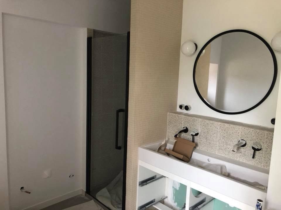 Meuble-lavabo moderne avec miroir rond, lavabo et porte de douche ouverte.