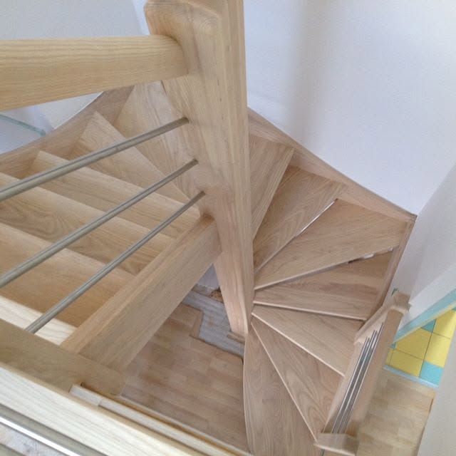 Escalier en colimaçon en bois avec rampes en métal dans un coin intérieur lumineux.