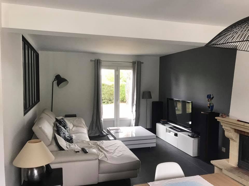 Salon moderne avec canapé gris, cheminée, télévision et portes-fenêtres ouvertes donnant sur un patio lumineux.