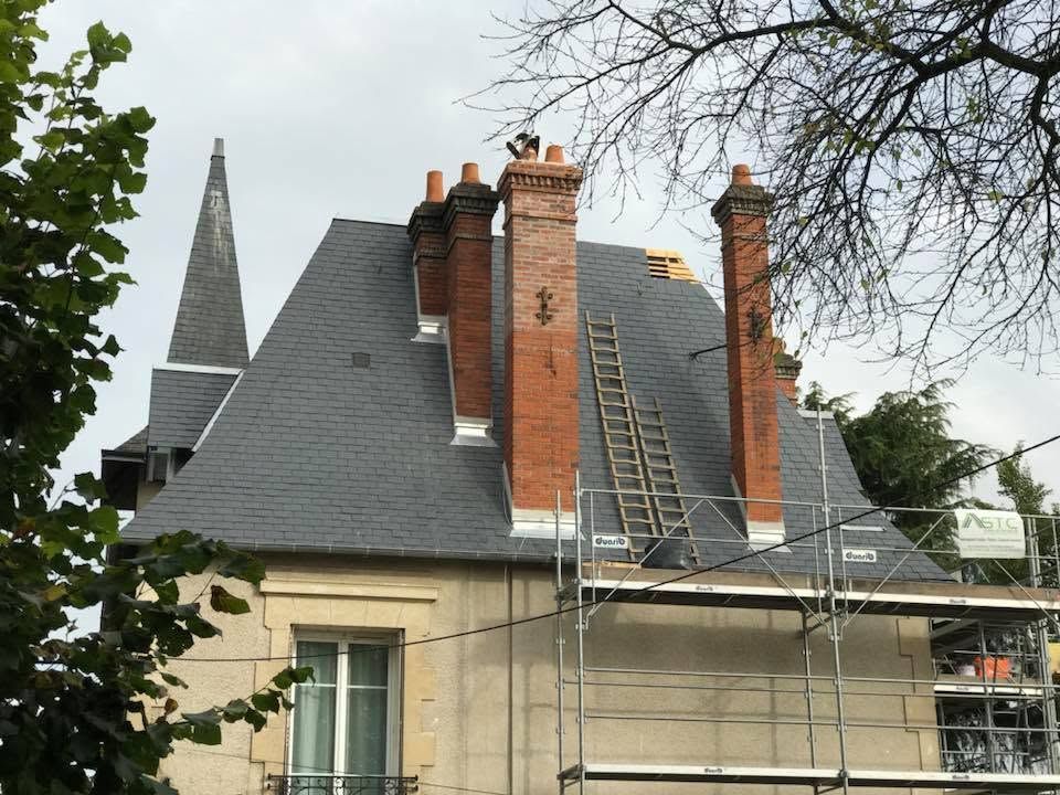 Toiture d'une maison en réparation, avec échafaudages et échelles, visible à côté du clocher d'une église.