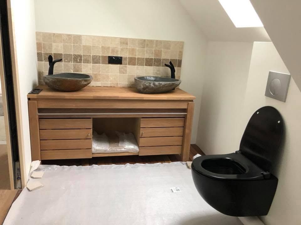 Salle de bains moderne avec meuble-lavabo en bois, deux vasques et toilettes noires sous un plafond mansardé.