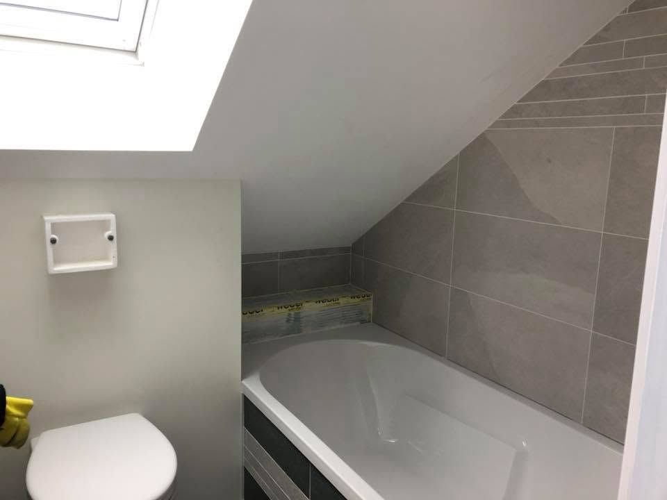 Petite salle de bains avec toilettes et baignoire sous un plafond mansardé et un puits de lumière.