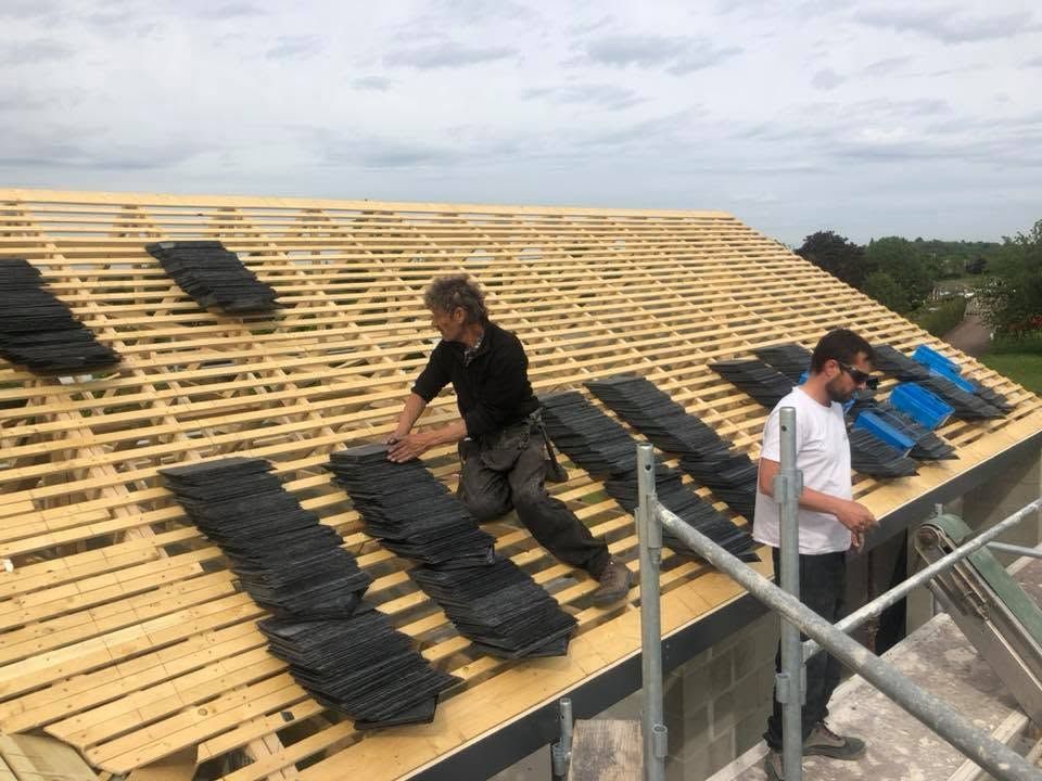 Des ouvriers posent des tuiles noires sur un toit en construction.