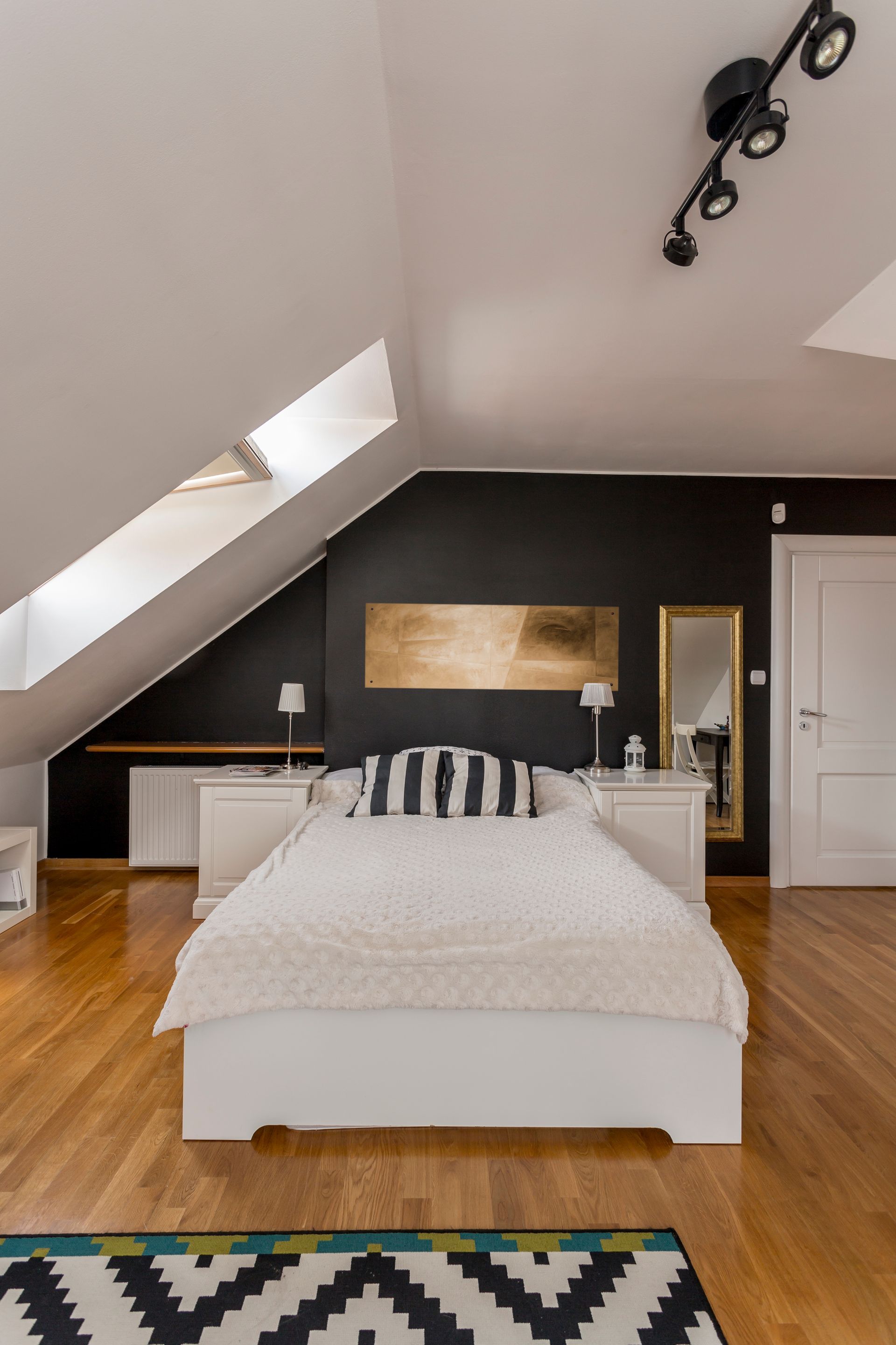 Chambre moderne avec un lit blanc, un mur d'accent noir, un plafond mansardé et un parquet.