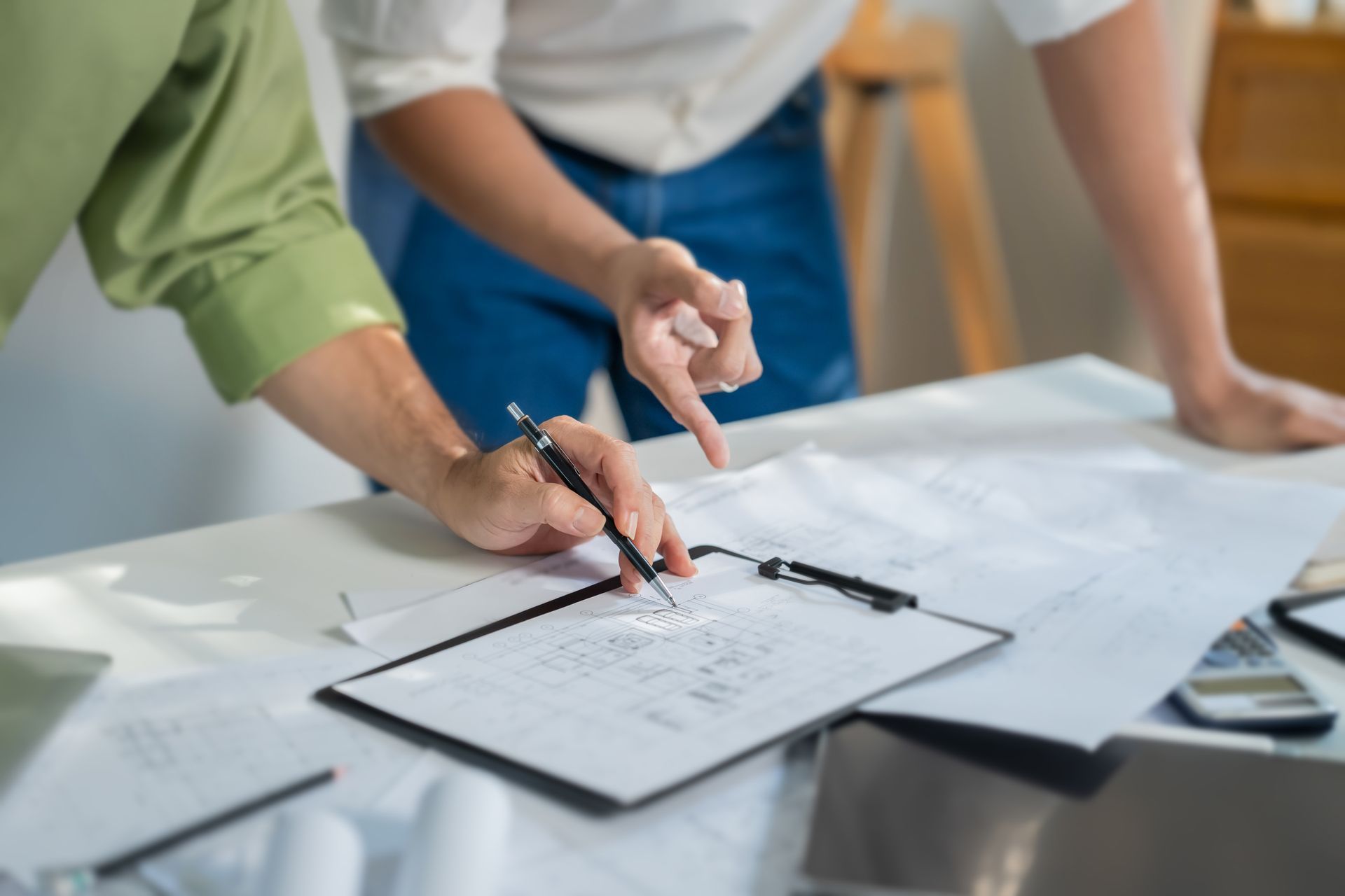 Des mains examinent un plan sur une table, des stylos et du papier à proximité.