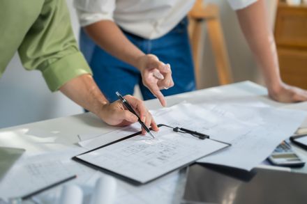 Des mains examinent des documents sur un bureau, un crayon et des graphiques étalés.