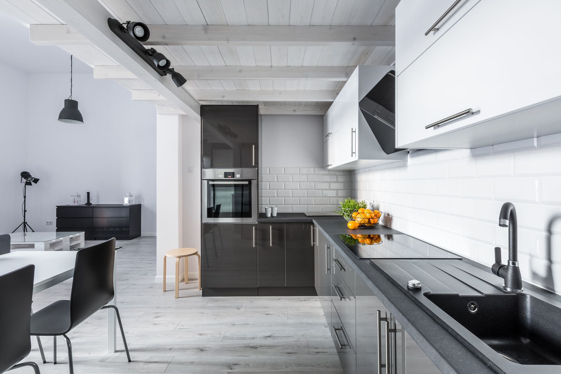 Cuisine moderne blanche avec armoires grises, comptoirs noirs et coin repas dans un loft lumineux.