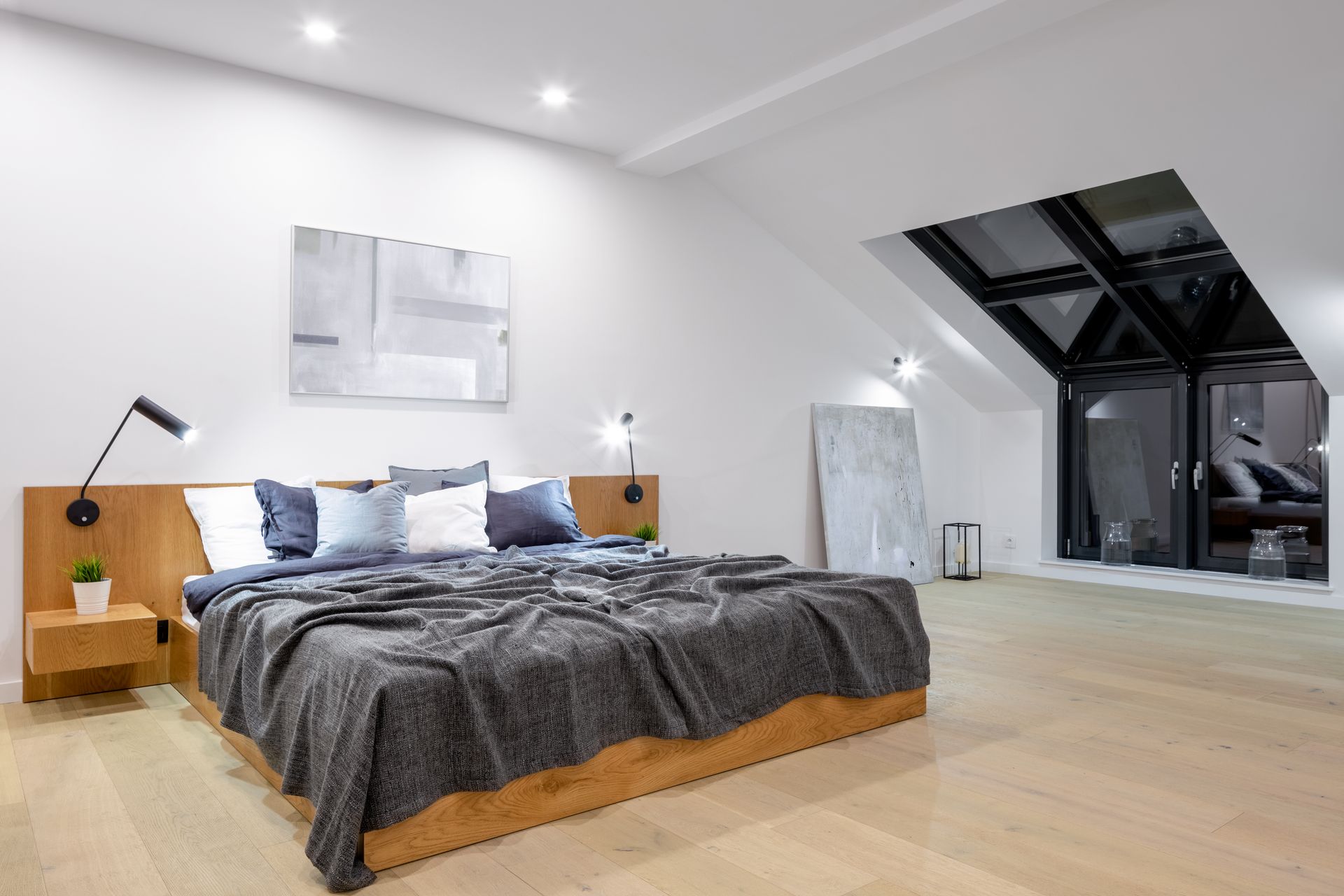 Chambre moderne avec un grand lit, du linge de lit gris, des lampes de chevet et une fenêtre inclinée donnant sur le ciel nocturne.