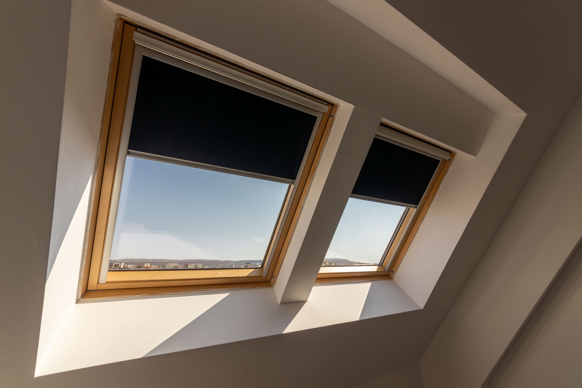 Deux fenêtres de toit dans un plafond blanc incliné, laissant apparaître le ciel bleu à l'extérieur.