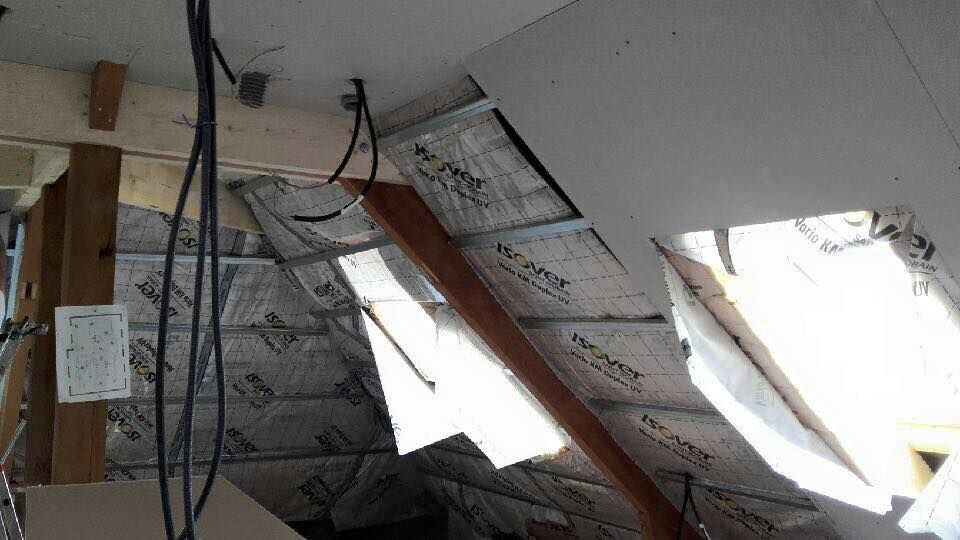 Plafond effondré avec isolation pendante et poutres apparentes dans une pièce intérieure.