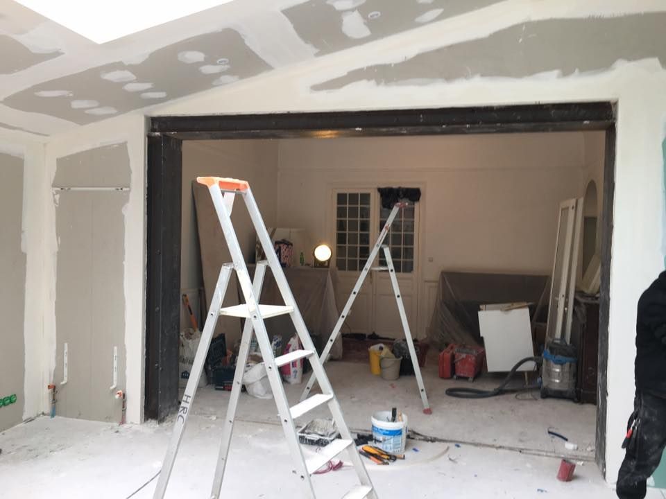 Garage en rénovation avec échelles, outils et cloisons sèches non finies autour d'une porte ouverte.