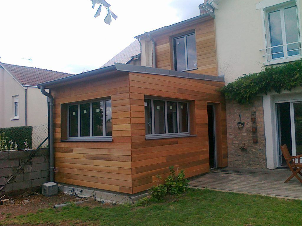 Maison moderne avec une extension en bois, des portes-fenêtres et un petit jardin gazonné.