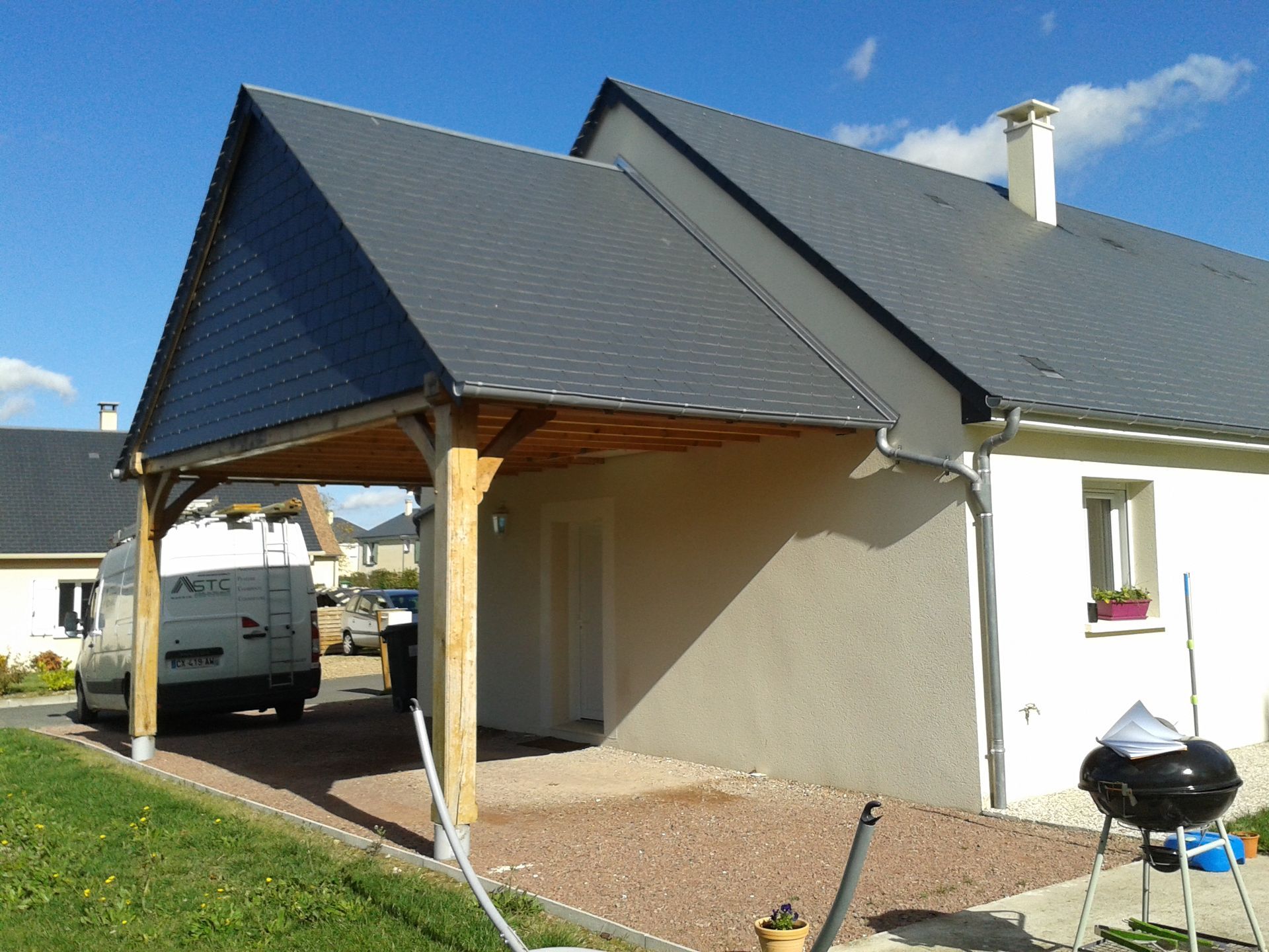 Maison moderne avec toit gris, abri voiture et fourgonnette blanche garée en dessous
