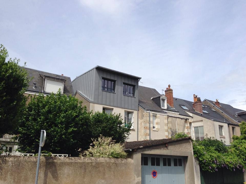 Rangée de maisons beiges aux toits en pente et à l'étage supérieur gris moderne sous un ciel nuageux.