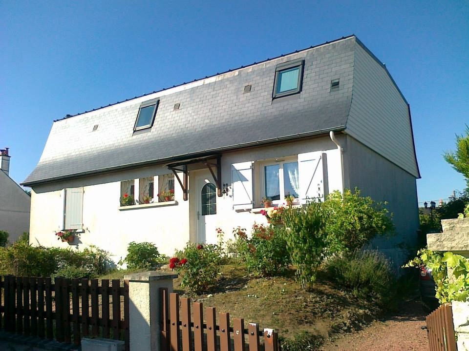Maison à deux étages avec bardage clair, toit foncé, jardin à l'avant et clôture en bois ensoleillée.