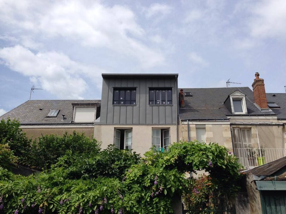 Rangée de maisons aux toits gris, une façade moderne centrale, se détachant sur d'épaisses haies vertes sous un ciel nuageux.