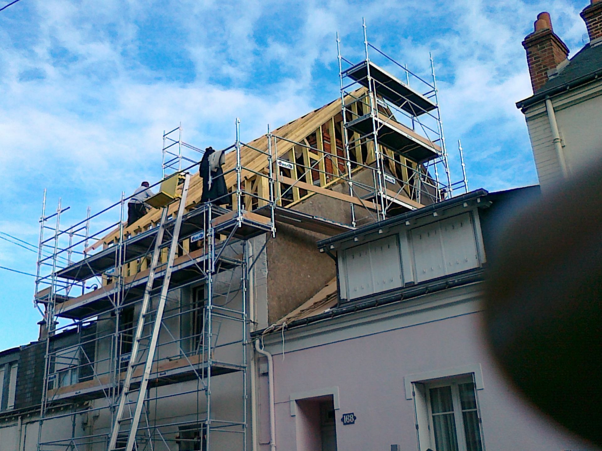 Échafaudages à côté du toit d'un bâtiment en briques en construction, sur fond de ciel bleu.