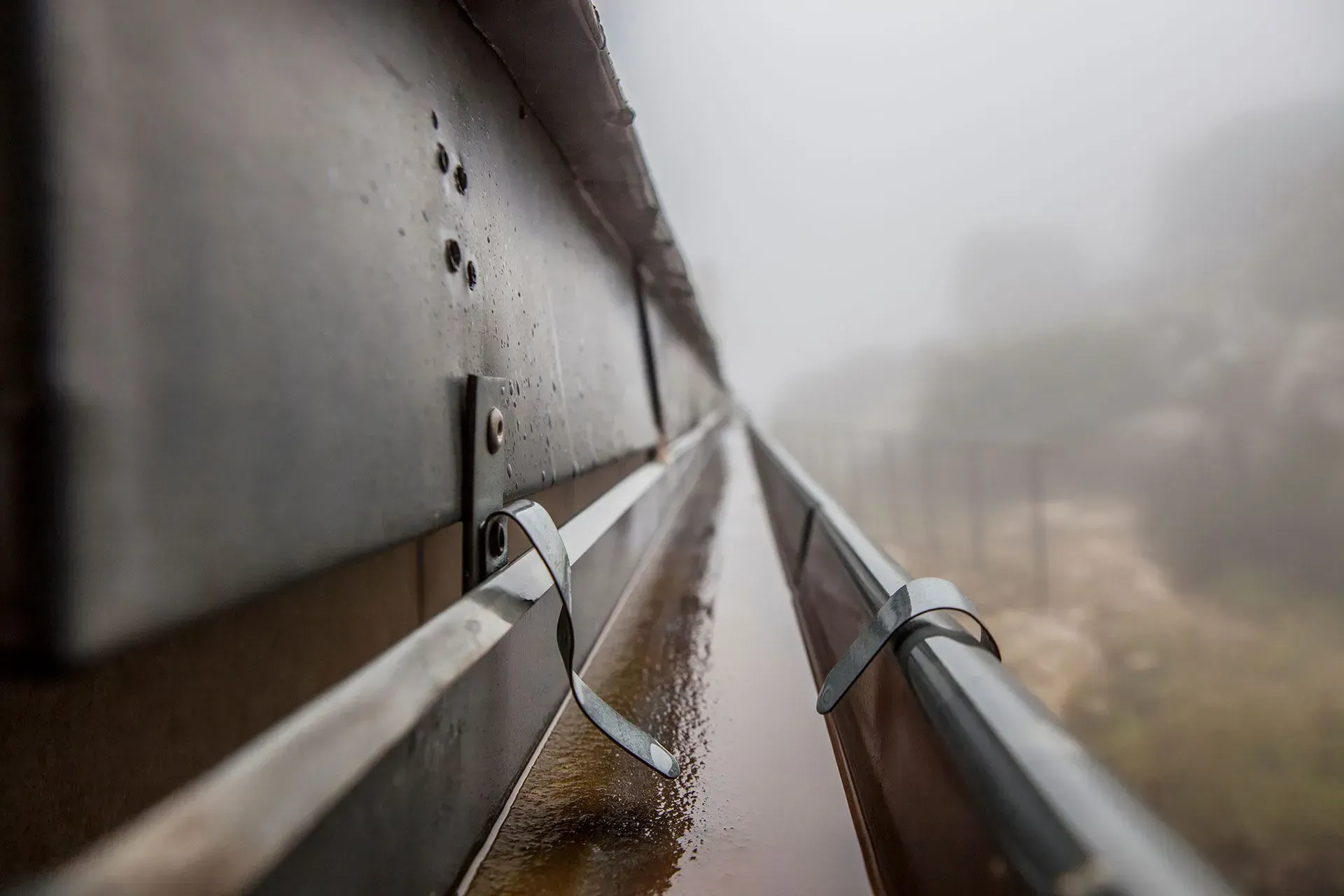 Rambarde métallique embuée, l'eau de pluie ruisselant le long d'un étroit rebord extérieur.