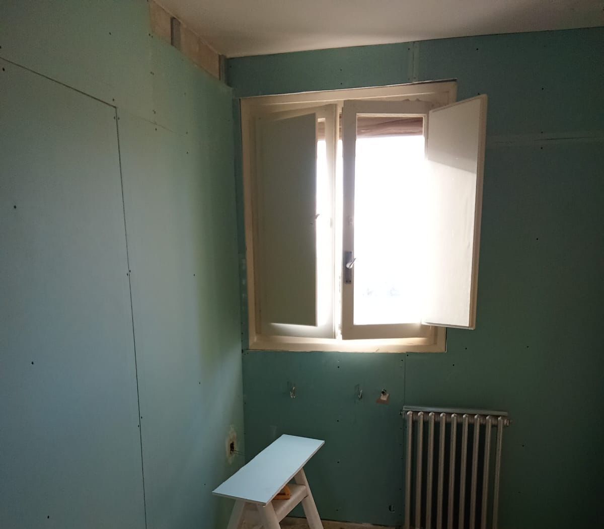 Una habitación con una ventana y un radiador y herramientas en el suelo.