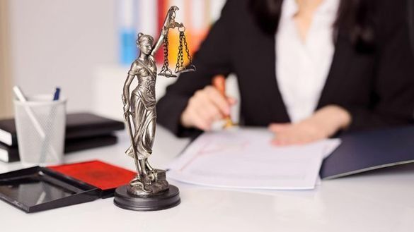 Una estatua de la justicia está sentada en un escritorio junto a una mujer que firma un documento.