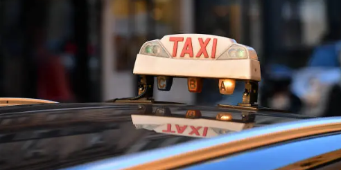 Gros plan sur une enseigne de toit de taxi avec des lettres rouges se reflétant sur le capot d'une voiture