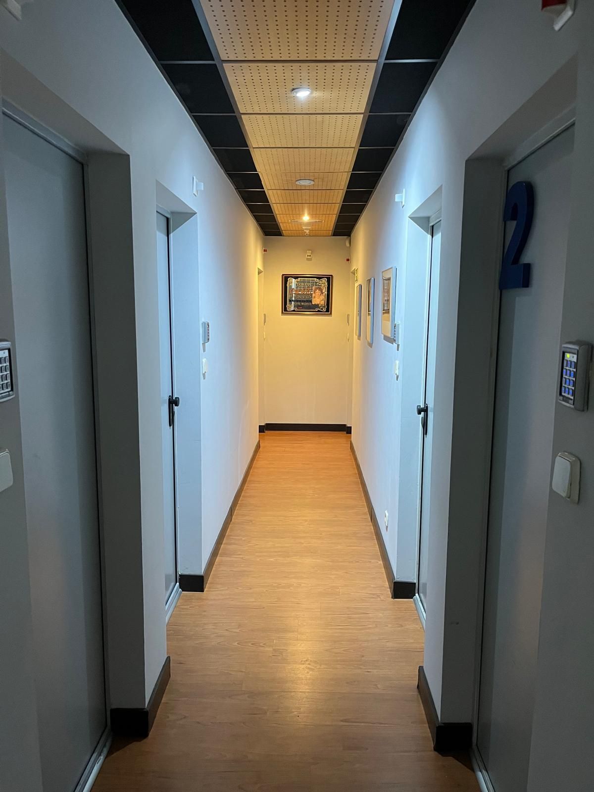 Pasillo estrecho con suelo imitación madera, paredes blancas, puertas a ambos lados y un cuadro al final.