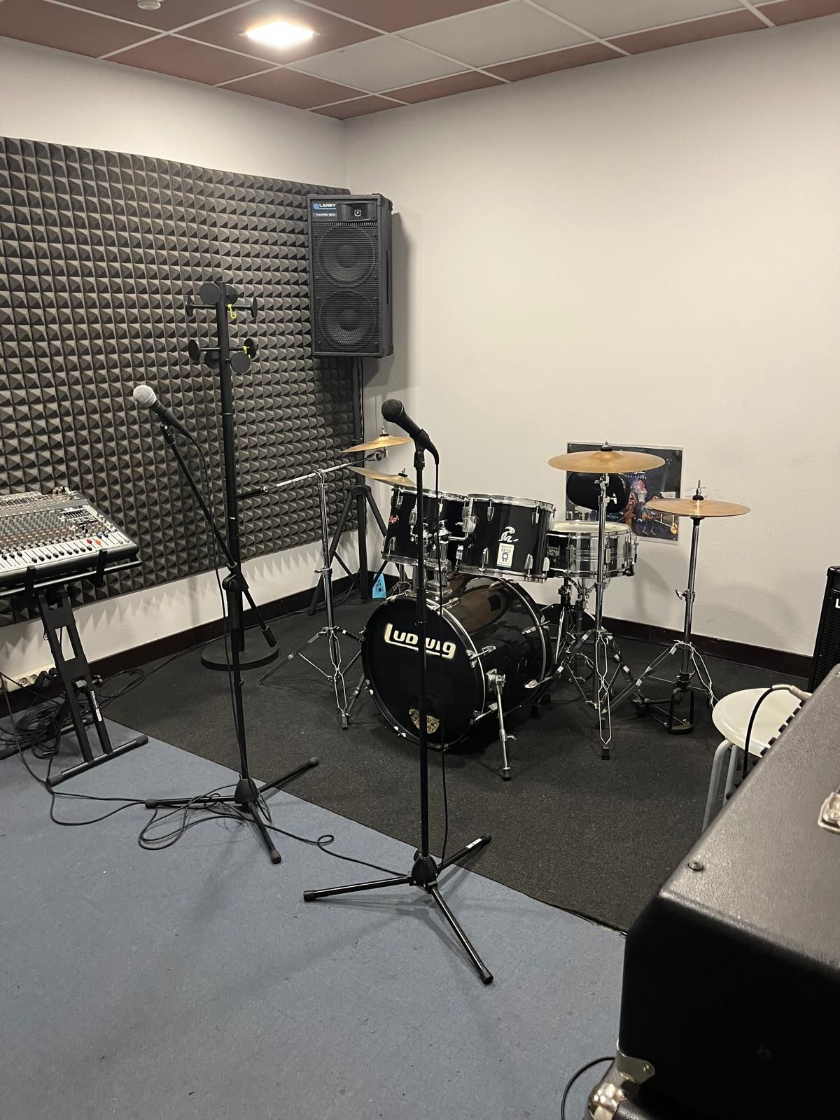 Batería y equipo en sala insonorizada con micrófonos y altavoces.