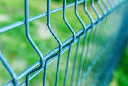 Un primer plano de una valla de alambre azul con un fondo verde.