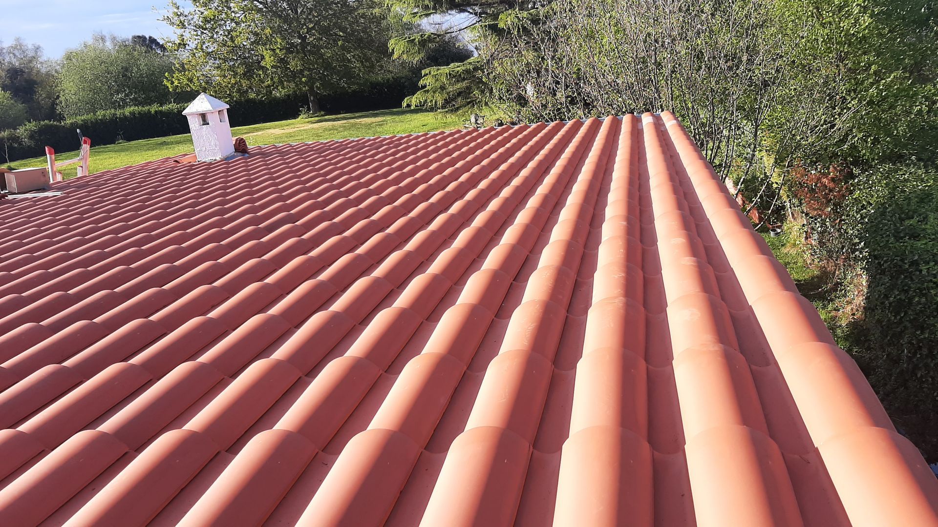 Un primer plano de un techo de tejas rojas con árboles al fondo.