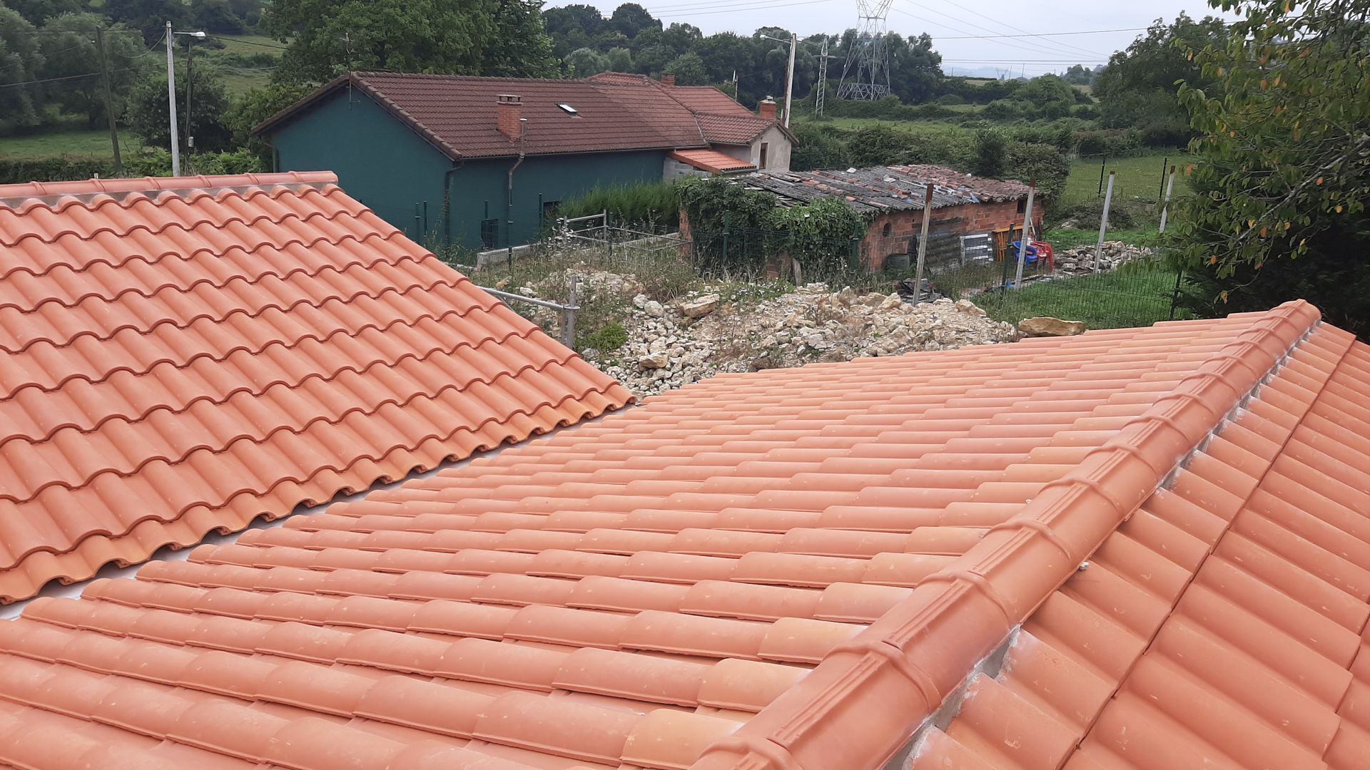 Un techo de tejas rojas con una casa verde al fondo.
