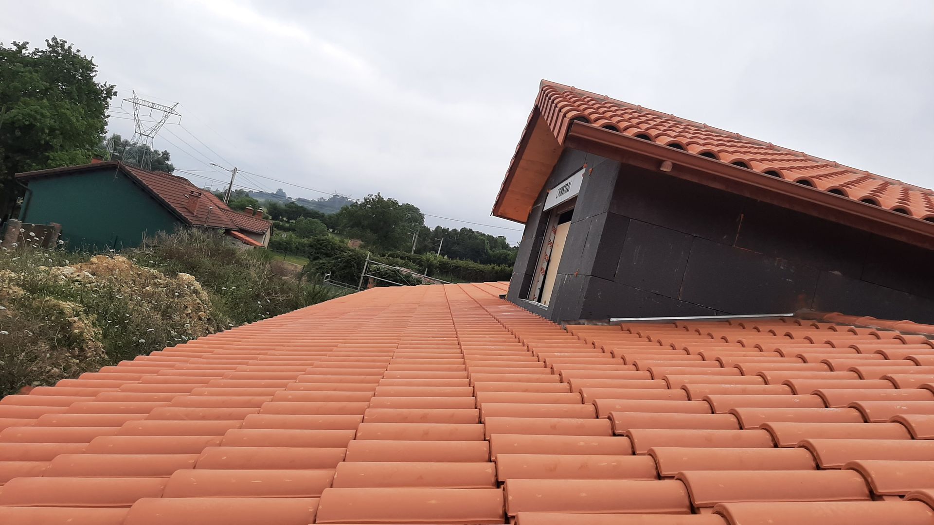 Un techo de tejas rojas con un edificio verde al fondo.